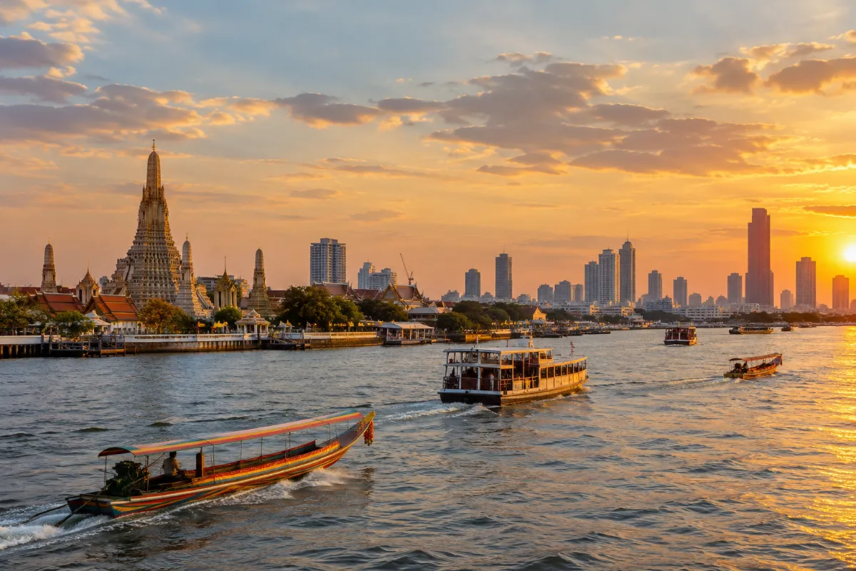 Floden Chao Phraya i Bangkok med färjor, tempeltorn och höghus i kvällsljus