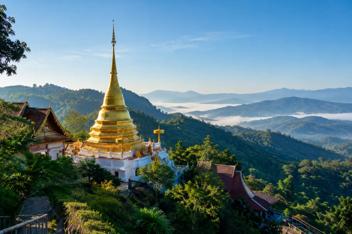 Buddhistiskt tempel med gyllene chedi på ett skogklätt berg i norra Thailand en klar morgon